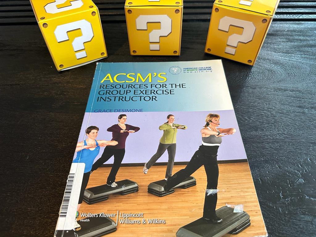 How to pick the best group fitness certification (Updated) 39 best exercise instructor certification - acsm group exercise textbook on table with yellow question mark boxes