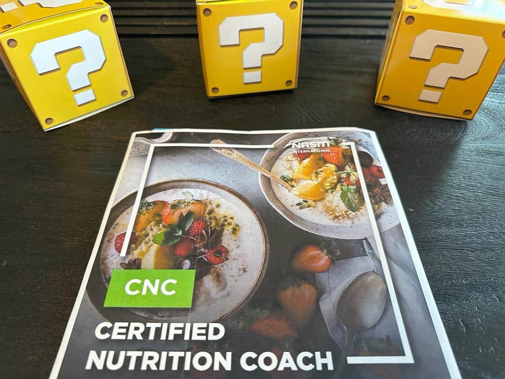 How to pick the best nutrition coach certification (Updated) 44 top Nutrition coaching certification - NASM CNC textbook laid out on table with yellow boxes with question marks