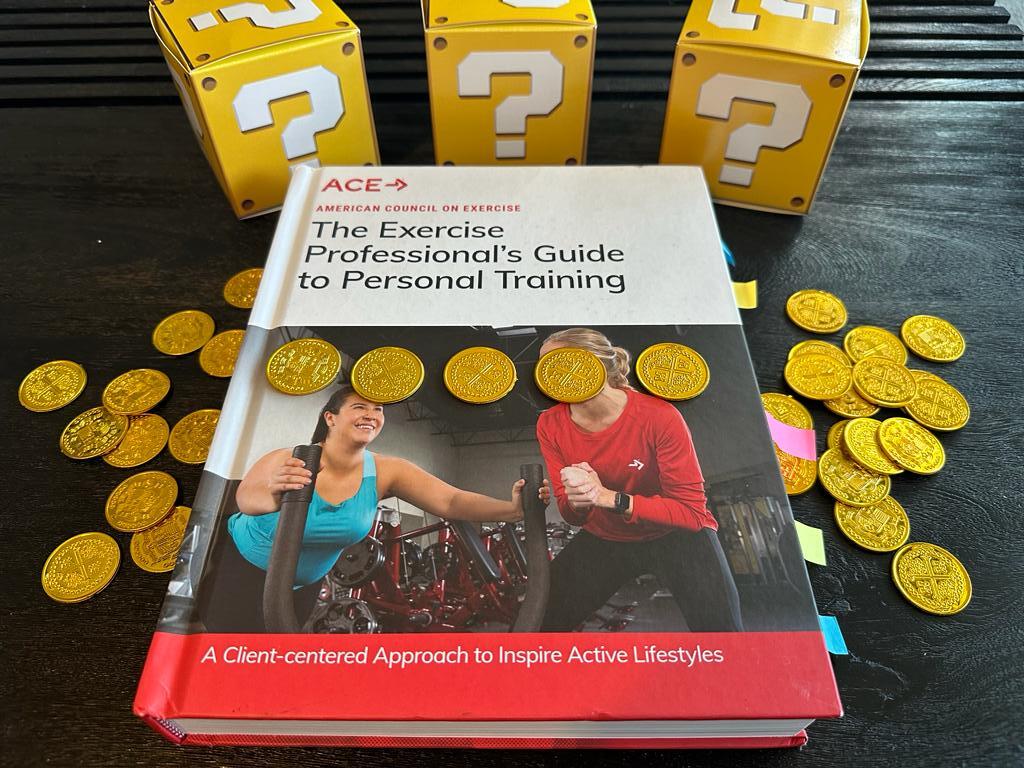 Cheapest personal trainer certification guide (Updated) 35 Cheapest personal training certifications - ACE textbook laid out on table with gold coins and mystery boxes - how much does ACE CPT cost?