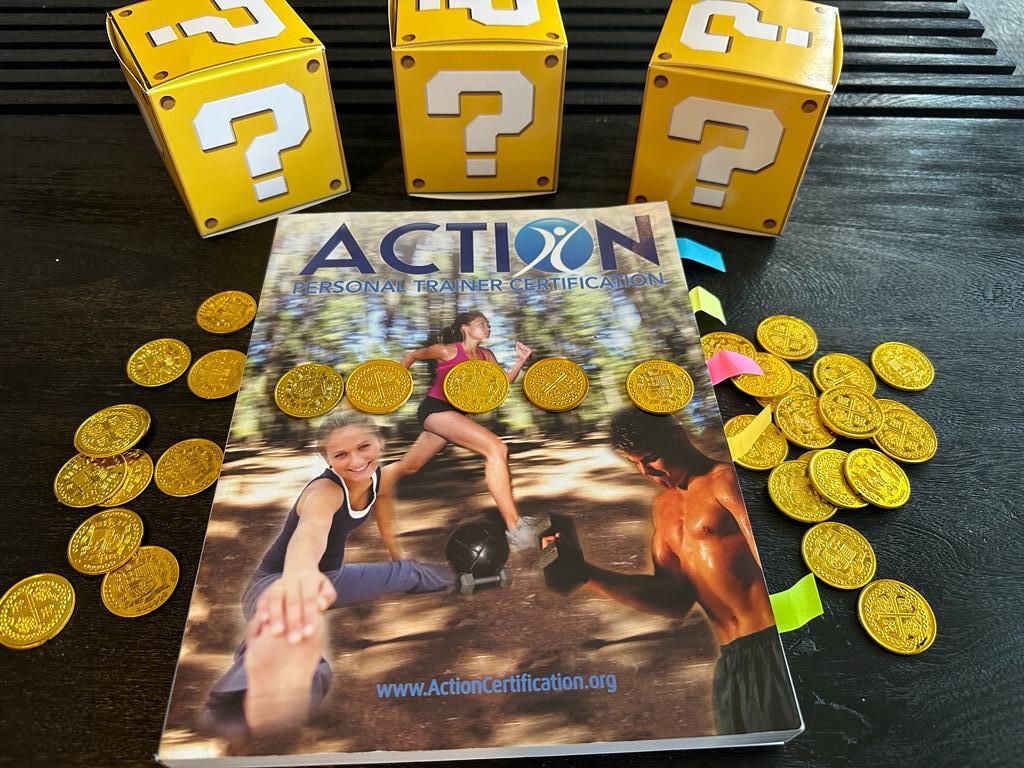 Cheapest personal trainer certification guide (Updated) 41 cheapest personal training certification - ACTION textbook laid out on table with gold coins and mystery boxes - how much does ACTION CPT cost?