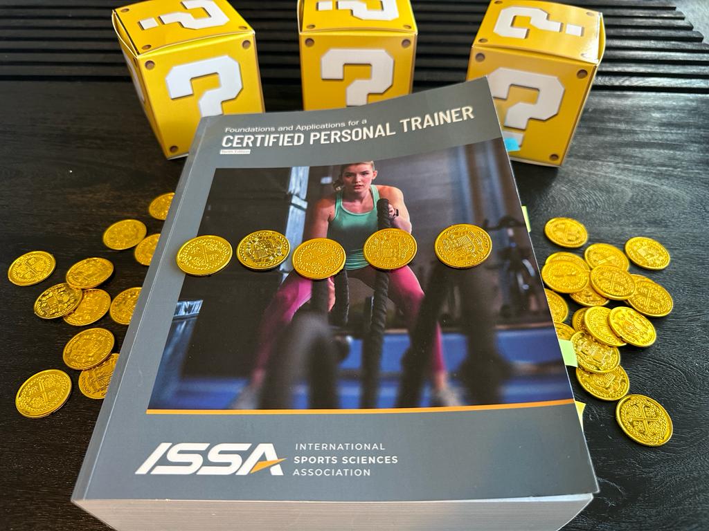 Cheapest personal trainer certification guide (Updated) 43 personal training certifications - NCCPT textbook laid out on table with gold coins and mystery boxes - how much does the NCCPT cost?