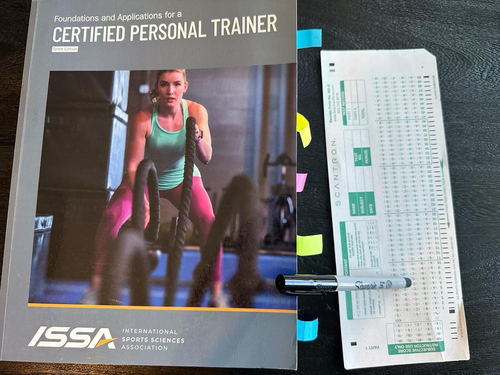 Easiest personal trainer certification guide (Updated) 31 Easiest personal training certifications - ISSA CPT textbook laid out with a copy of scantron exam next to it and a sharpie