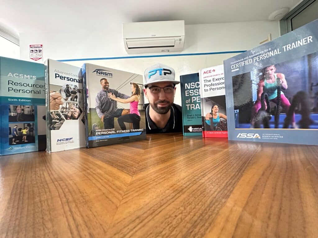 Updated: How to pick the best personal trainer certification 31 Best Personal Training Certifications - Tyler stands up personal training textbooks on a table from ACSM, NCSF, NASM, NSCA, ACE, ISSA