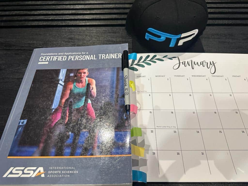 FREE ISSA Study Plan, Study Calendar + Blueprint 4 ISSA Study plan - ISSA textbook with calendar laid on table with ISSA CPT notes to plan ISSA exam prep