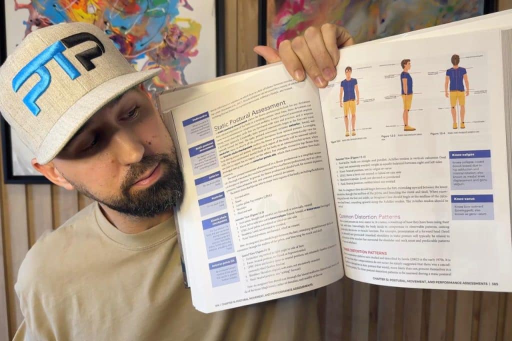 Tyler Read holds up a copy of the NASM CPT textbook looking at the page covering the static postural assessment
